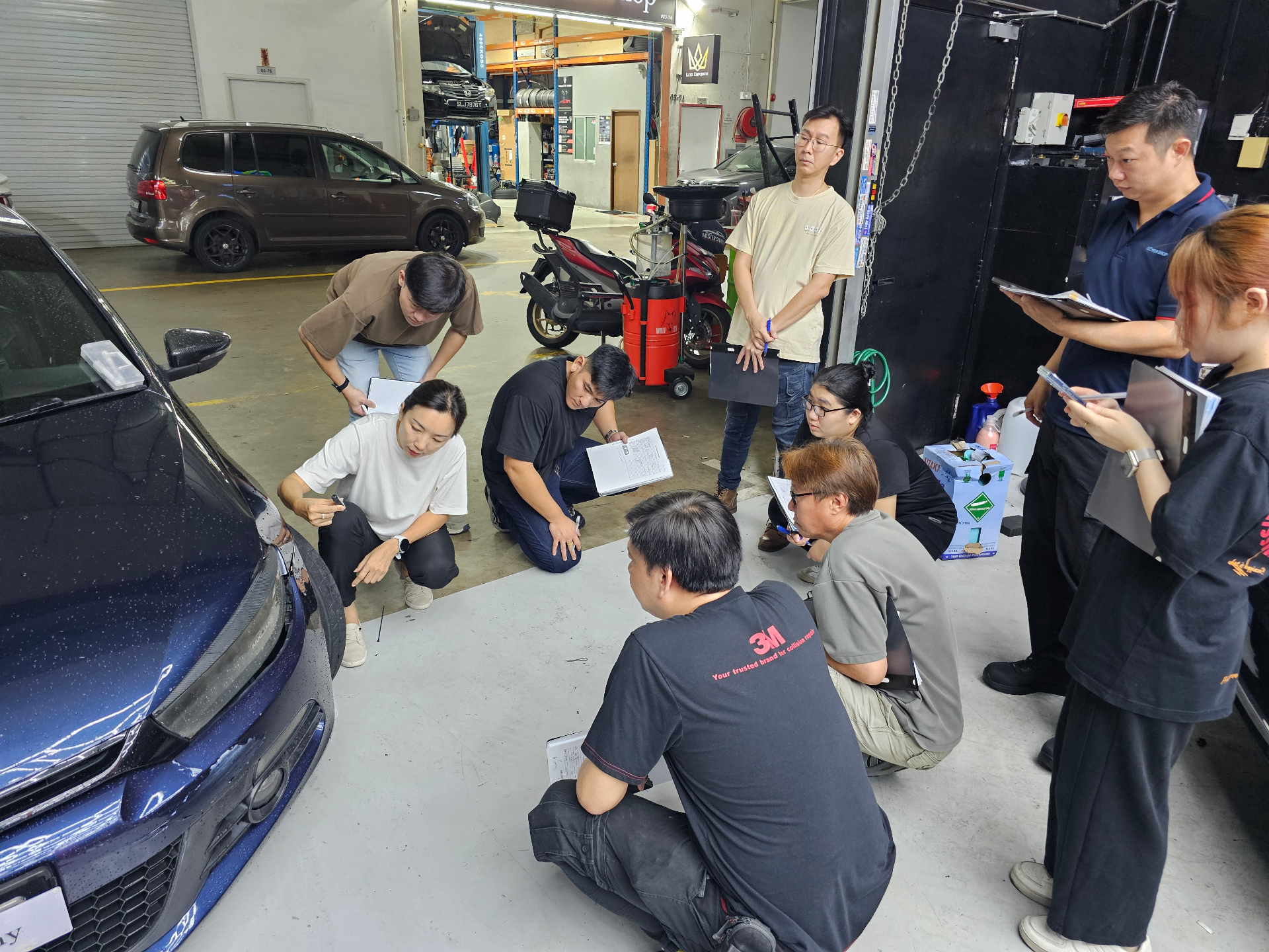 Igive trainer guiding participants through vehicle damage assessment in a workshop.